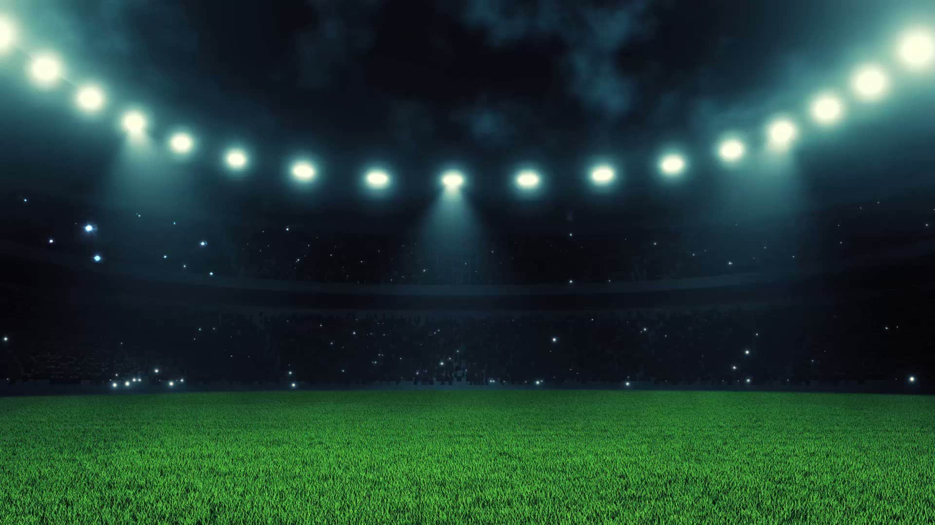 A brightly lit, empty stadium at night, showing a green grass field under circular stadium lights with a dark sky in the background.